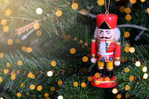 istock Toy funny nutcracker hanging on Christmas tree. New Year, holiday background with place for text, flare and bokeh lights. Soft selective focus. Front view. Horizontal 1284605967