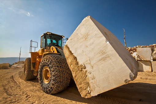 Bulldozer carrying oversized marble block in marble quarry