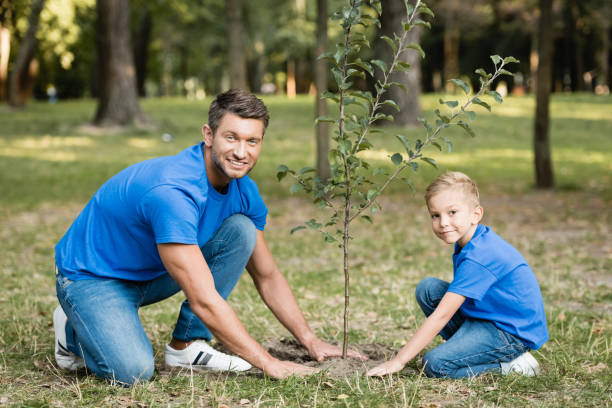 istock smiling father and son looking at camera while planting young tree in forest, ecology concept 1284608706