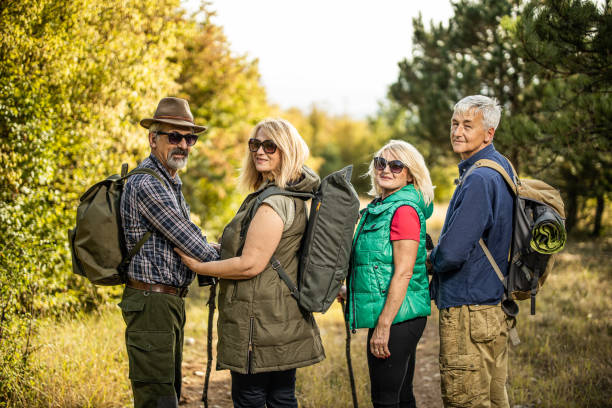 istock Two senior couples with backpacks standing in a row on dirt road and posing during hiking 1284611333