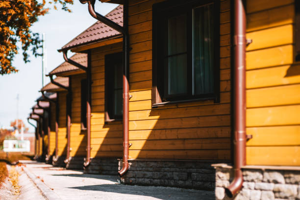 The row of wooden yellow houses A row of yellow equal regular wooden single-story houses in a youth hostel or boarding house with triangle roofs, downpipes, and single windows, sunny day, shallow depth of field, selective focus summer camp cabin stock pictures, royalty-free photos & images