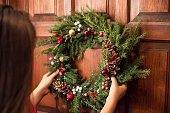 Back view of a young girl, hanging a christmas wreath on the door of her home.