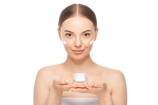 portrait of young woman holding face cream jar with both hands, standing with naked shoulders, isolated on white background - clear sky human skin women smiling imagens e fotografias de stock