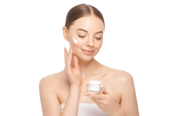 young beautiful female with closed eyes applying face cream to cheekbones as part of morning routine, isolated on white background - clear sky human skin women smiling imagens e fotografias de stock