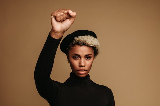 African american woman protesting against racism with raised fist. Portrait of african american woman in cap with a raised fist.