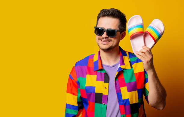 style guy in 90s shirt and pixel sunglasses holds flip flops on yellow background style guy in 90s shirt and pixel sunglasses holds flip flops on yellow background flip flop sandal beach isolated stock pictures, royalty-free photos & images