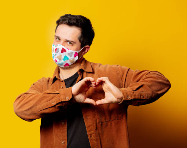 istock Guy in face mask show heart gesture on yellow background 1284619179