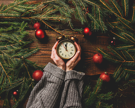 Female hands hold alarm clock next to Christmas decoration