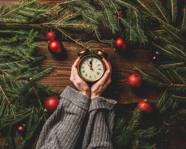 Female hands hold alarm clock next to Christmas decoration stock photo