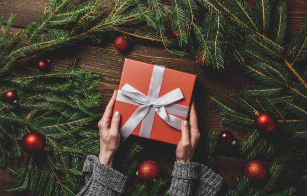 istock Female hands hold gift box next to Christmas decoration on a table 1284619489