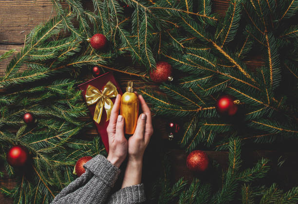 istock Female hands hold perfume bottle next to Christmas tree branches and baubles around 1284619493