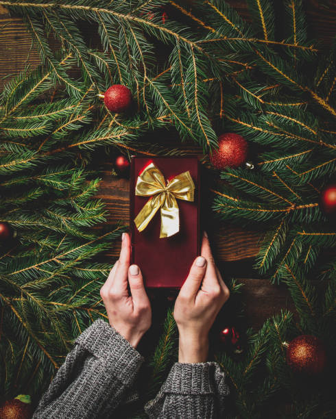 istock Female hands hold gift box next to Christmas tree branches and baubles around 1284619535