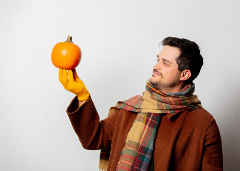 Style man in coat and scarf with pumpkin on white background