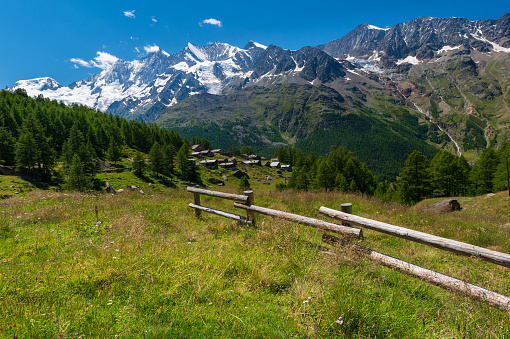 Old little wooden houses along the road on the green hill with the impressive Mischabel massif and white alpine peaks Täschhorn, Dom, Lenzspitze, Nadelhorn, Stecknadelhorn, Hohberghorn, Dürrenhorn and glaciers.