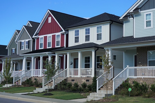 Middle-class, suburban neighborhood showing a row of multicolored row houses built in 2018 in North Carolina. The houses are two-story with porches and a small grass front yard.