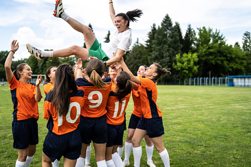 Group of female football player celebrating victory together with their female coach. Coach is in the air.