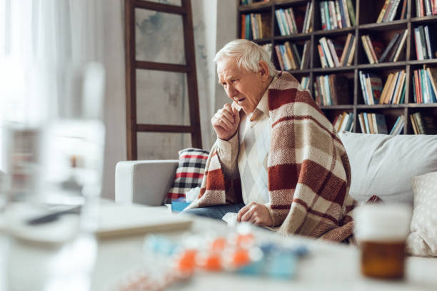Senior man alone sitting at library covered with plaid coughing