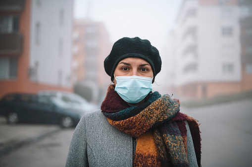 Portrait of beautiful woman wearing winter clothes standing outdoor with protective face mask during COVID-19 pandemic.