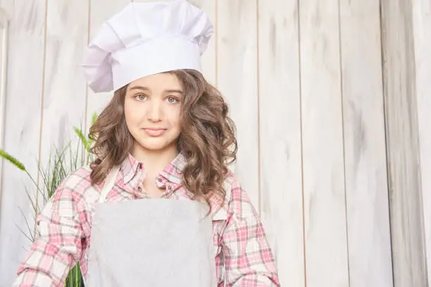 Beautiful girl. Little cook. White cap. Brown curly hair.
