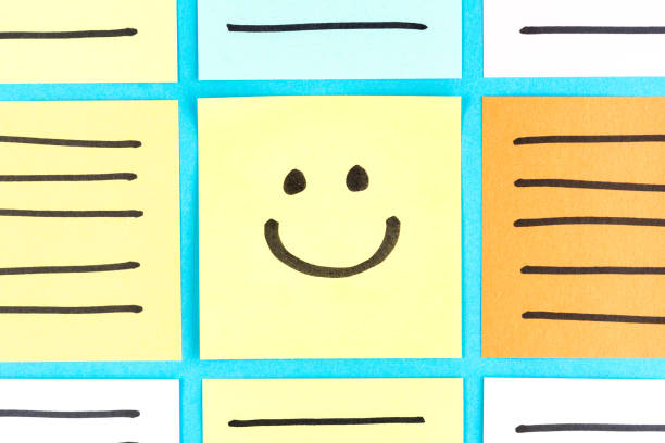 Adhesive notes with a drawing of a happy smiling emoticon on a yellow paper and blue background. Hapiness concept. Adhesive notes with a drawing of a happy smiling emoticon on a yellow paper and blue background. Hapiness concept. smiley face postit stock pictures, royalty-free photos & images