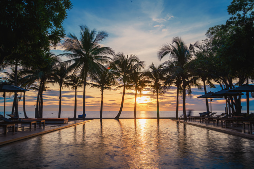 Silhouette of carefree woman relaxing at the infinity pool on the beach at sunset. Copy space.