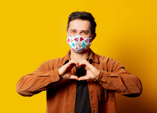 istock Guy in face mask show heart gesture on yellow background 1284653960