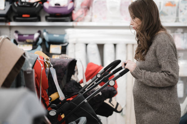 Young pregnant woman carefully choosing infant baby stroller or pram buggy for newborn. Pregnancy and shopping. Shopping for expectant mothers and baby. Young pregnant woman is of baby store in mall stock photo