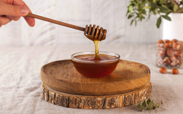 brown honey in a glass bowl on a rustic wooden plate. the wooden spoon drips slowly. - sweet food chestnut yellow brown imagens e fotografias de stock