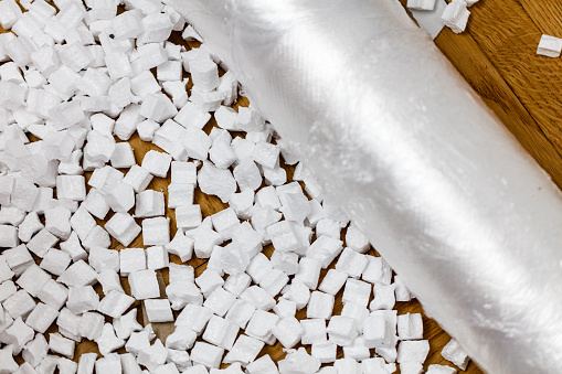 White packing peanut and roll of plastic wrapping foil on parquet floor