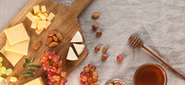 Cheese plate. Assorted cheeses on a wooden Board with grapes, honey, nuts on a linen tablecloth. Copy space.