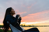 湖の夕日の間に自然の中で熱い飲み物を楽しむ若い女性