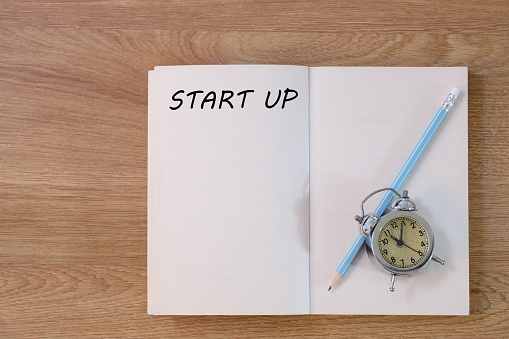 Start up concept on notebook with pencil and clock on wooden table. Business concept.