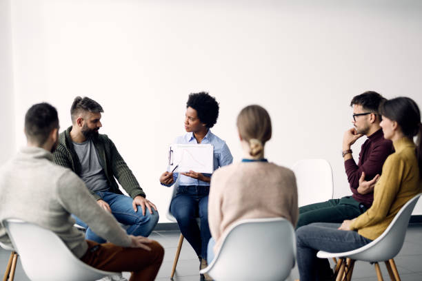 istock African American psychotherapist analyzing progress with group of people during a session. 1284684213