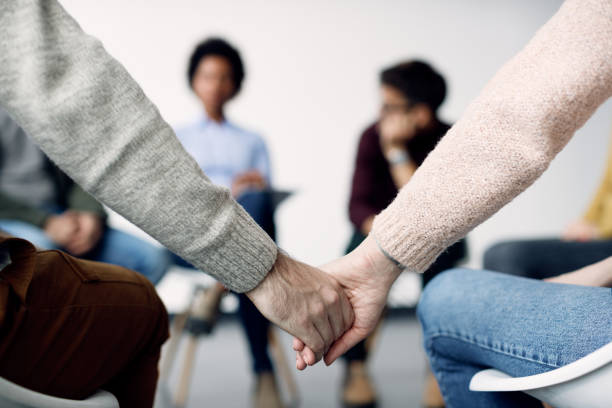 istock Close-up of two people holding hands during group therapy. 1284684372