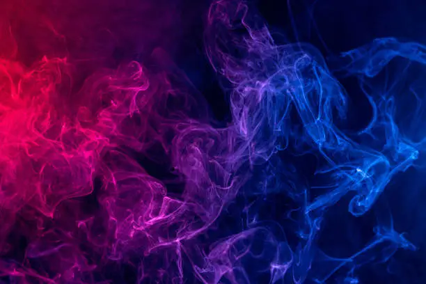 Photo of Conceptual image of colorful red and blue color smoke on dark black background.