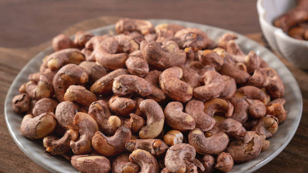 istock Cashew nuts with peel in a plate on wooden tray. 1284686732