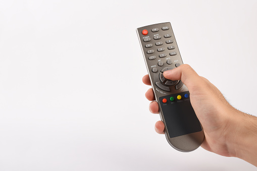 Men's hand holding TV remote control, men's finger pushing TV remote control button on the white background with copy space