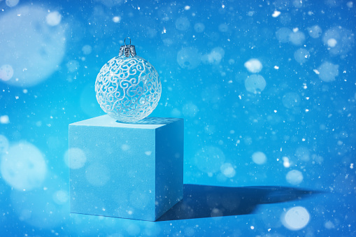 delicate beautiful white Christmas tree ball on a blue background. falling snow. New Year, Christmas