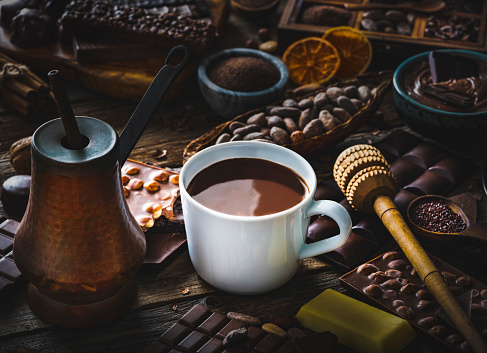 Melted chocolate cup with vintage copper chocolate pot and cocoa beans with assorted bars on rustic wood