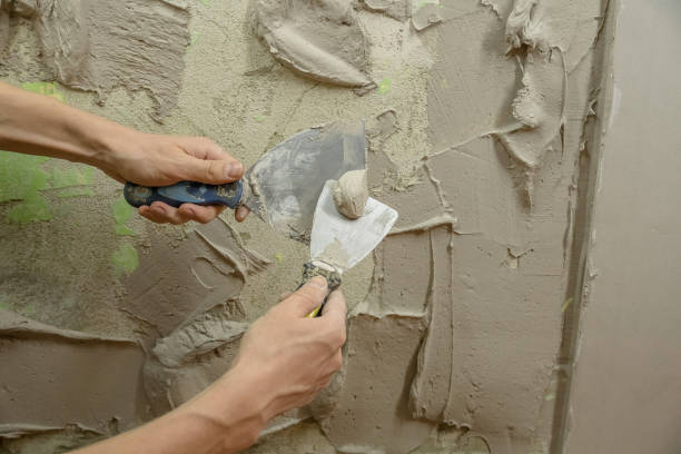 istock A worker plasters the wall with a spatula and applies a cement mix solution. The repairman lays the plaster on the drywall. Handyman repairs home. Laborer restore dwelling. Specialist covers up cracks 1284692895