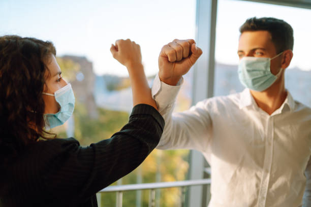 istock Business colleagues in protective face masks bumping elbows while greeting each other near elevator at modern office. Covid-19. 1284699434