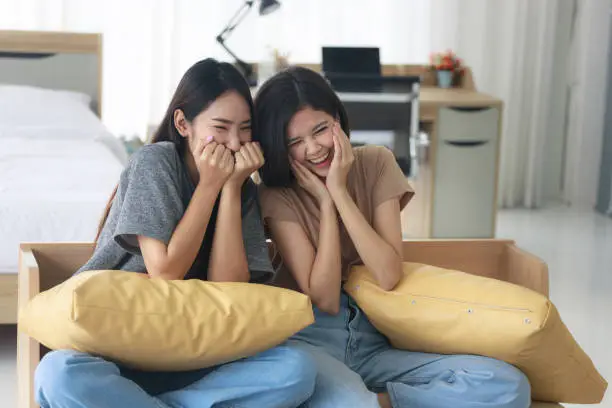 Two Asian teenage girls are Intimate friends with short and long hair they are happy to watch movies and series from TV in the bedroom. Young women are enjoying leisure activities.