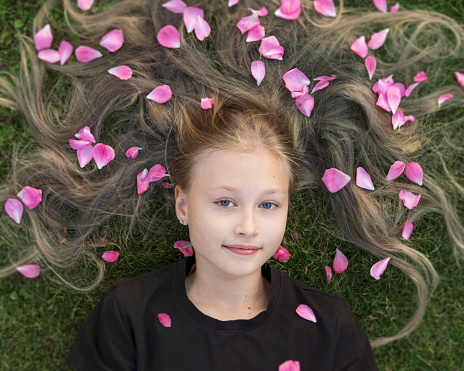 Portrait of a beautiful blonde girl with a smile, lying on the grass with rose petals in her hair.