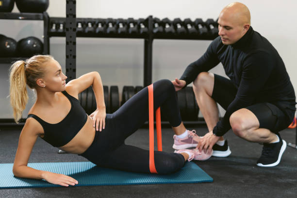 istock Young woman performs glute bridging with elastic band resistance on gym workout with personal trainer. The concept of a private training session in a small sports studio 1284702536