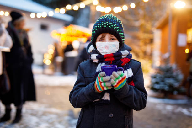 kid boy drinking hot children punch on german christmas market. happy child with medical mask . people with masks as protection against corona virus. covid pandemic time in europe and in the world. - hot chocolate hot drink heat drinking imagens e fotografias de stock