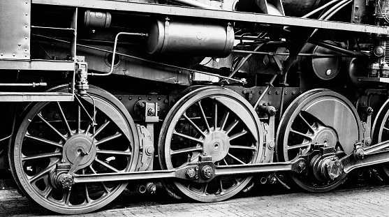 Old vintage steam locomotive wheels detail in black and white close up. The iron driving wheels are powered by the locomotive's pistons.