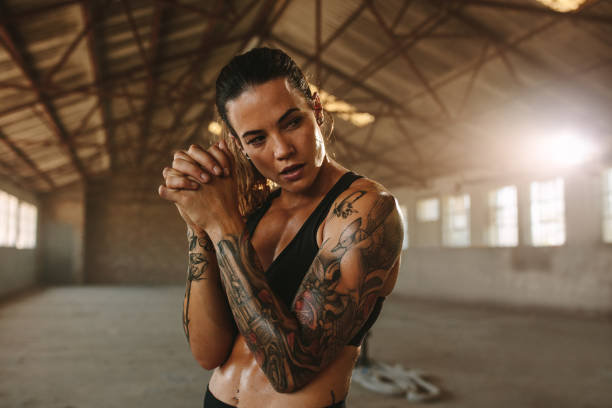 Fitness woman standing inside old factory. Tattooed woman after workout session in old warehouse.