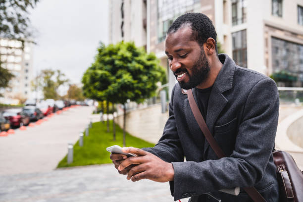 istock Nice-looking african 30s man using his phone during city walk in elegant coat 1284712849