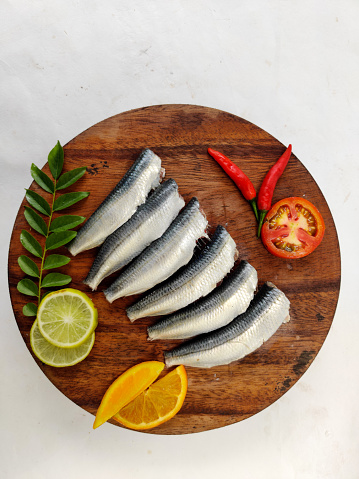 Limpiado y listo para cocinar sardina india fresca decorada con hojas de curry, rodaja de limón y rodaja de tomate. Aislado sobre fondo blanco. photo
