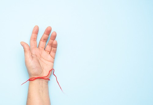 red woolen thread on the wrist of a female hand, blue background, copy space